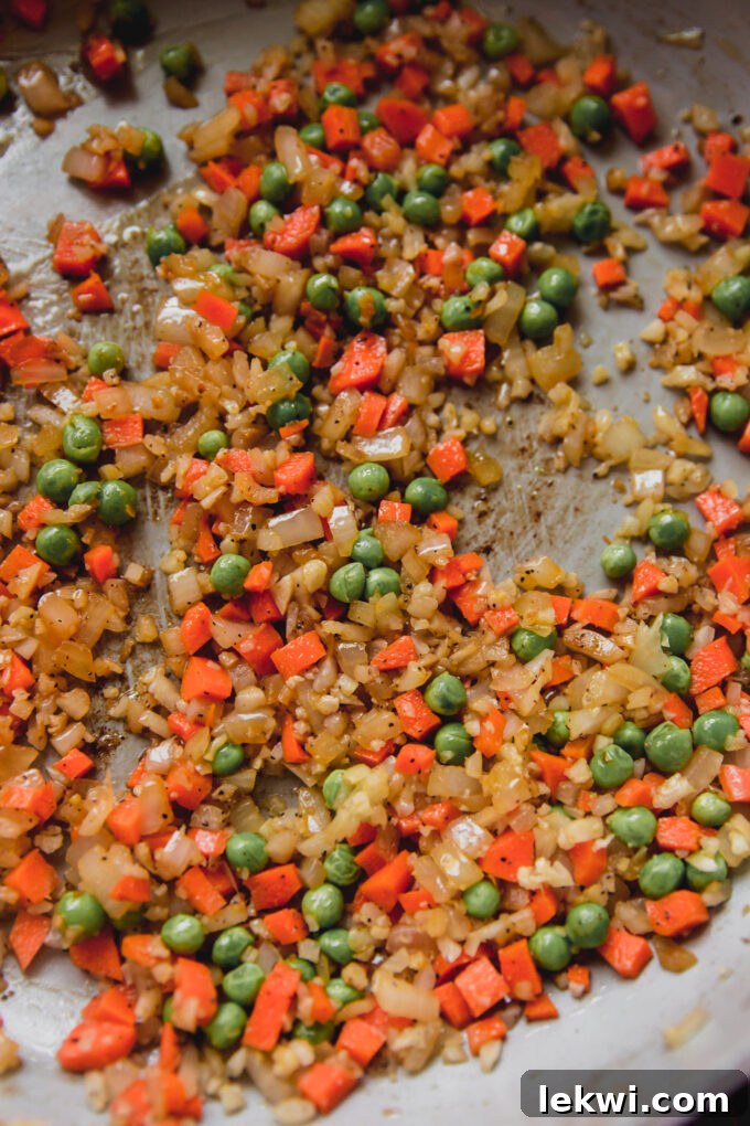A vibrant mix of carrots, onion, cauliflower rice, and peas sautéing in a pan, ready for the rice.