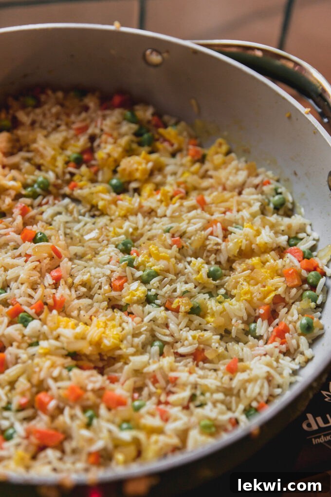 Cooked fried rice with scrambled egg, peas, and carrots fully mixed in, still in the pan.