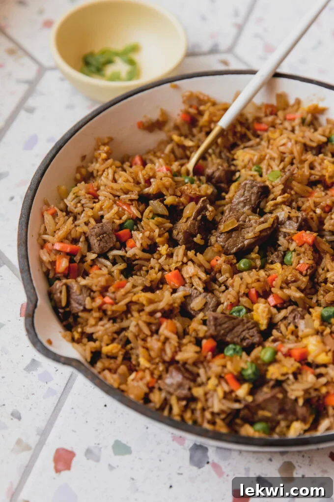 Steak fried rice cooking in a white pan, with a serving spoon dipping into the delicious mixture.