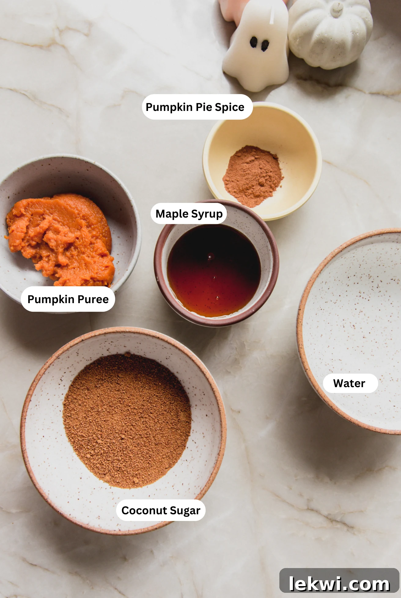 Various ingredients for pumpkin spice syrup laid out in small bowls, including pumpkin puree, spices, and sweeteners.