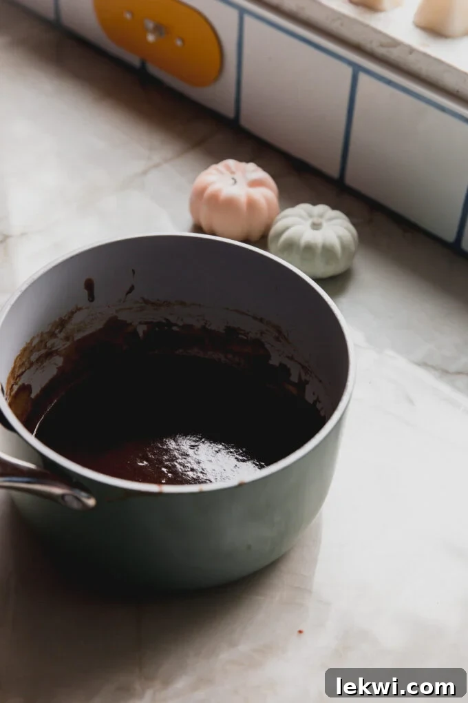 A pot of simmering pumpkin spice syrup with festive pumpkin-themed candles in the soft-focus background.