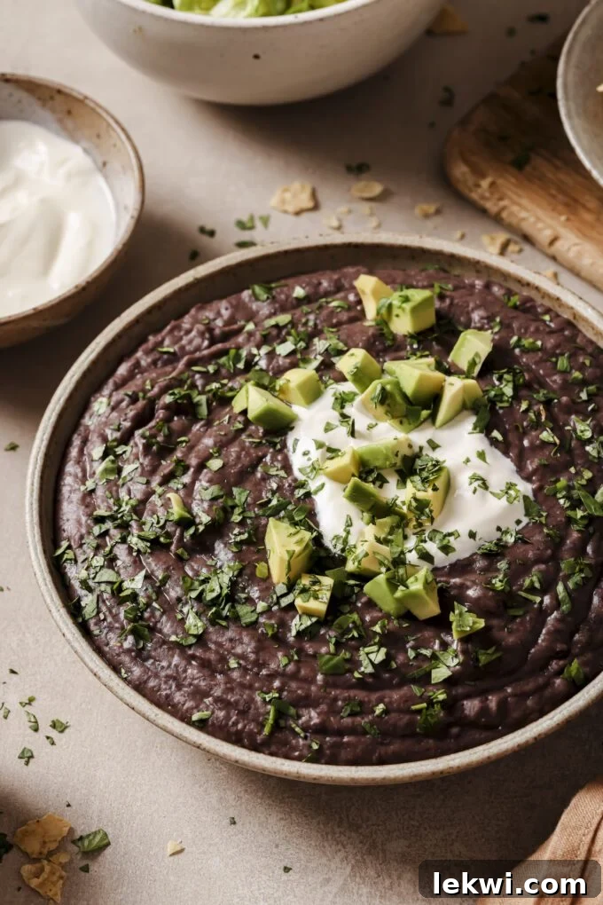 Cooked refried beans in a bowl topped with avocado and chopped cilantro.