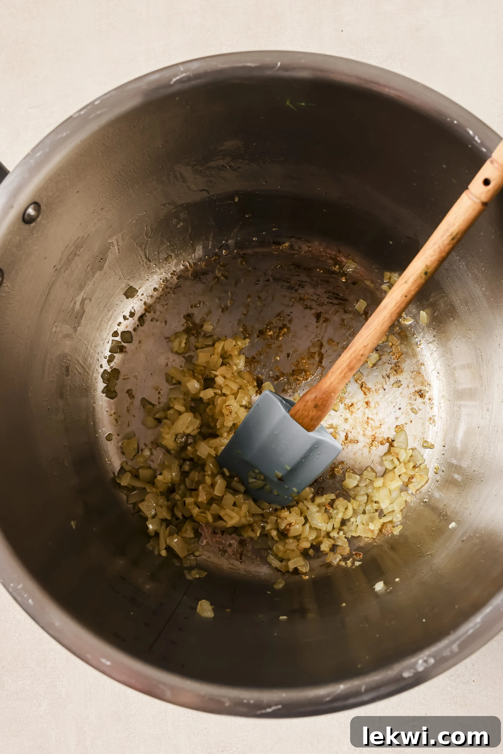 Onions sautéing in a pressure cooker with a spoon.