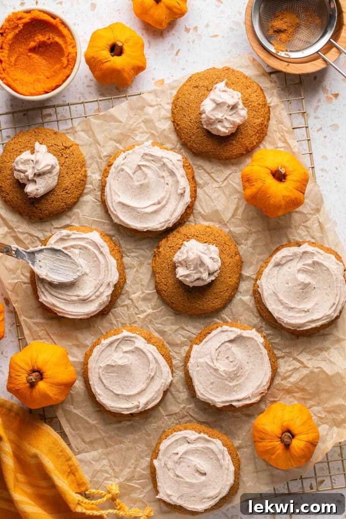 A freshly baked pumpkin cookie on a wire rack being frosted with creamy latte icing, demonstrating the spreading process.