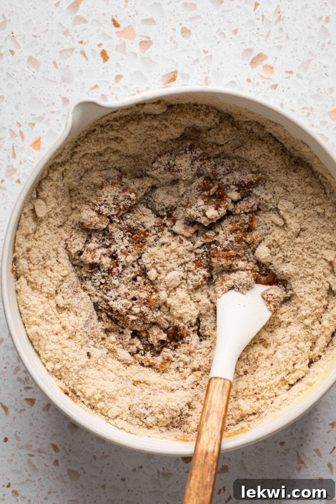 Wet and dry pumpkin spice cookie ingredients being gently whisked together in a bowl to form a cohesive dough.