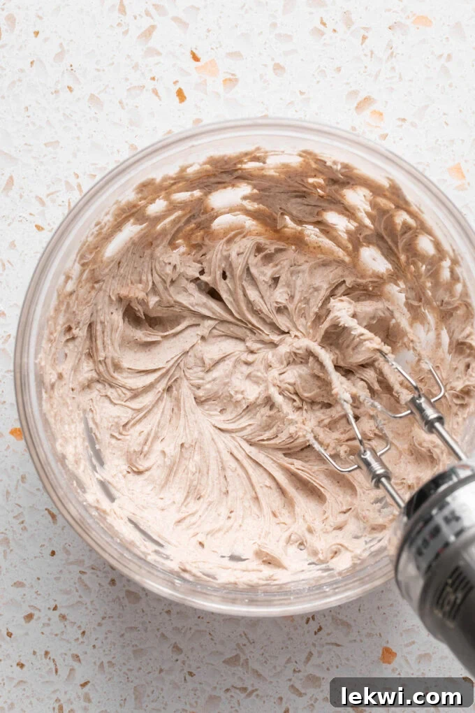 Pumpkin spice icing ingredients actively being whisked in a bowl, transforming into a smooth and creamy frosting.