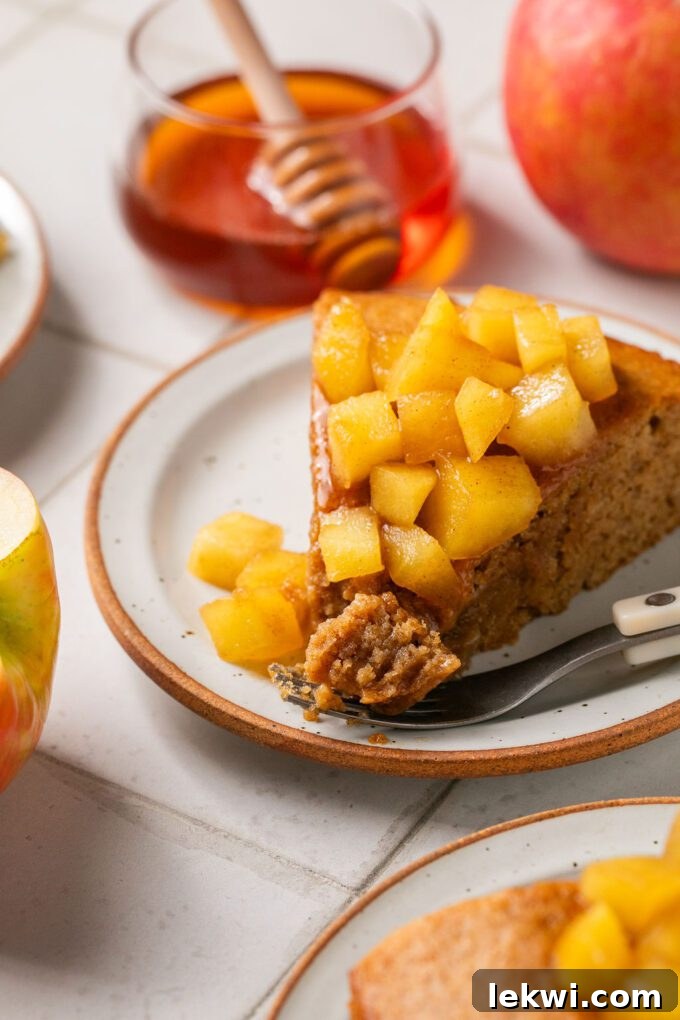 A beautifully presented slice of gluten-free honey apple cake, topped with caramelized apple pieces and a drizzle of honey.