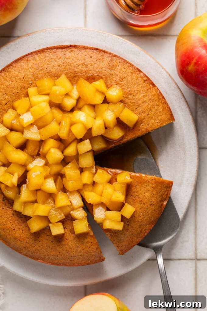 A slice of gluten-free honey apple cake removed from the whole cake, showcasing its moist texture and abundant apple topping.