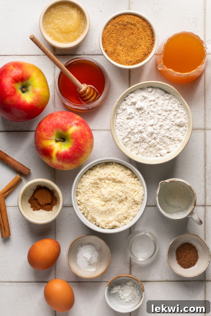 Ingredients for a gluten-free honey apple cake, including flours, honey, apples, and spices, are neatly arranged on a rustic wooden surface.