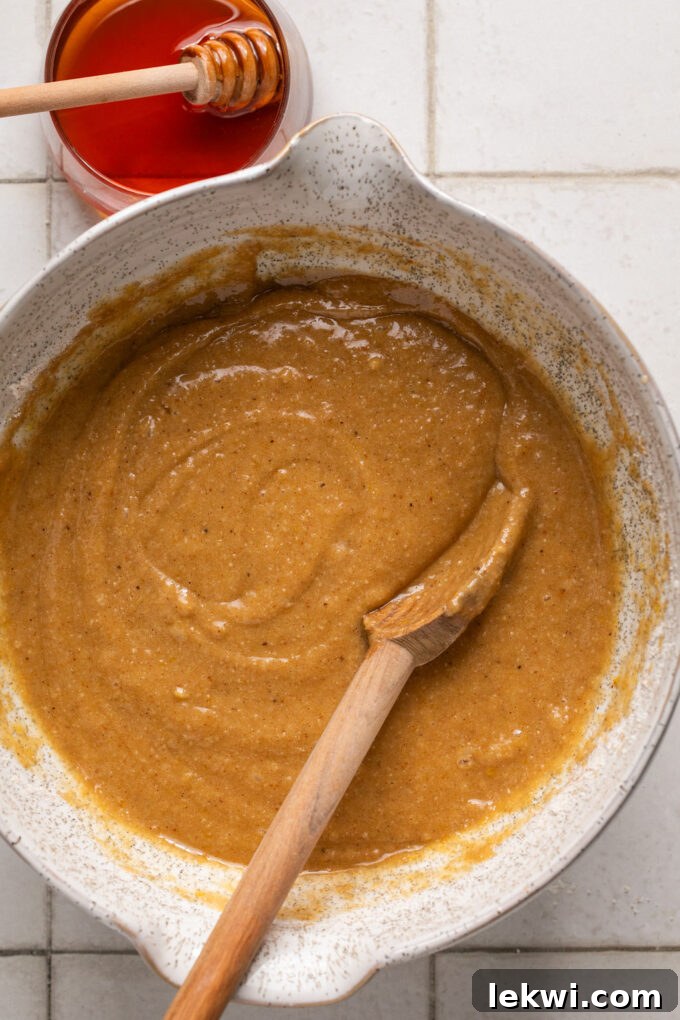 Smooth honey apple cake batter resting in a mixing bowl with a spoon, ready for baking.