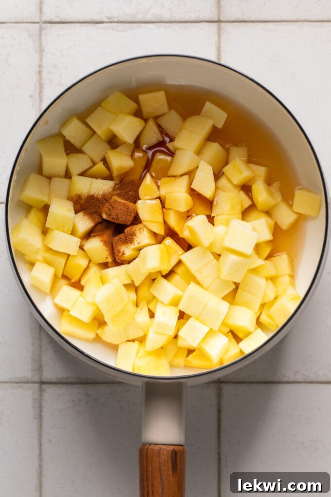 Diced honey crisp apples, honey, and cinnamon uncooked in a small pot, ready to be simmered for the topping.