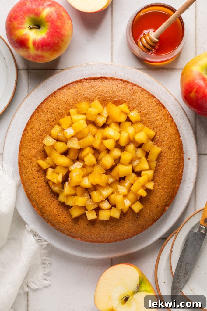 A freshly baked gluten-free honey apple cake generously topped with caramelized apples, presented on a large ceramic plate.