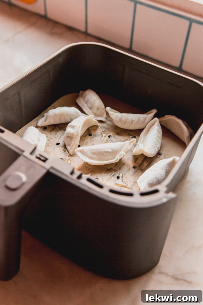 Uncooked gluten-free dumplings arranged neatly in an air fryer basket lined with parchment paper.