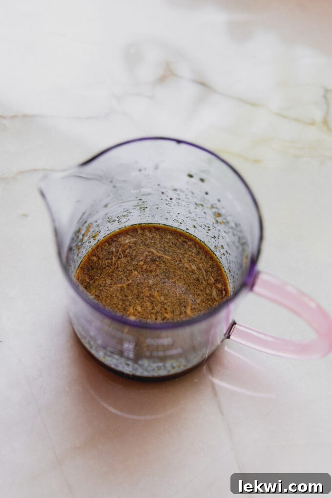 A measuring cup containing the freshly made coconut aminos-based almond ginger dressing, ready to be poured.