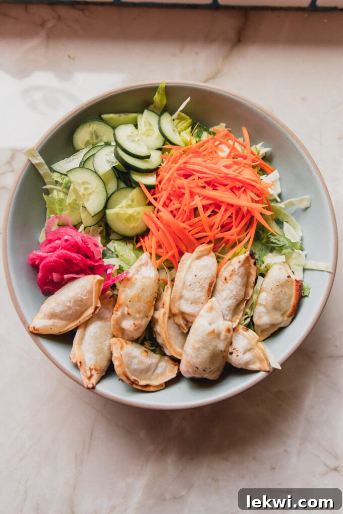 A bowl showcasing the vibrant mixture of potstickers, fresh lettuce, shredded carrots, chopped cucumber, and red onion, before dressing is added.
