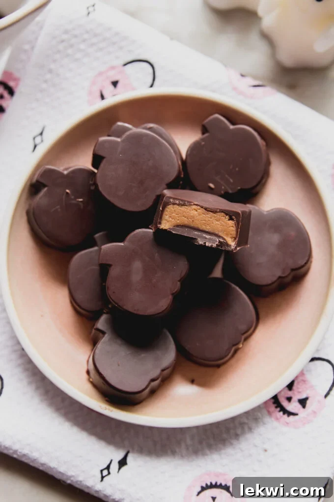 Almond butter cups shaped like pumpkins on a pink plate, with a bite taken from one. A perfect Halloween treat.