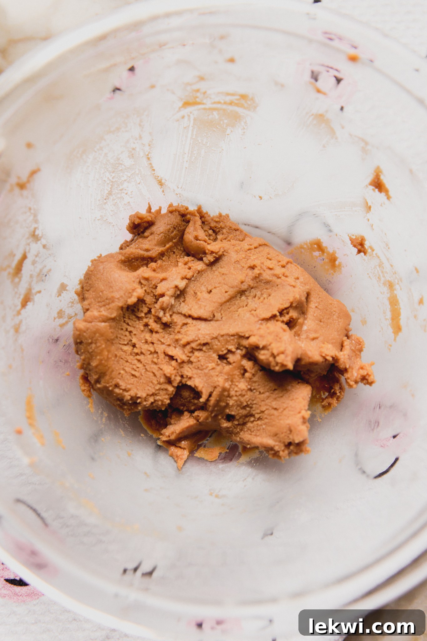Almond butter, maple syrup and coconut flour mixed in a bowl, forming a smooth, moldable dough for the filling.