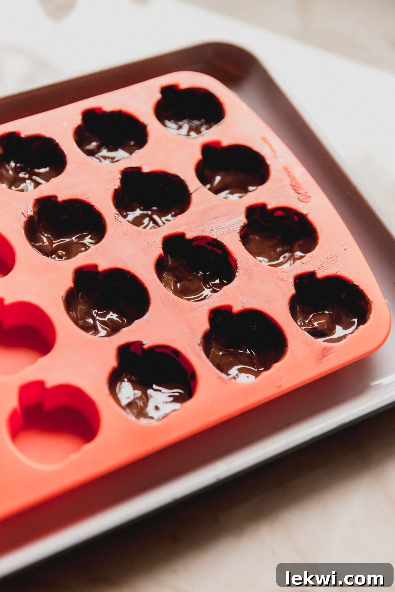 Pumpkin mold with melted chocolate coating the inside of 12 spaces, forming the base of the cups.