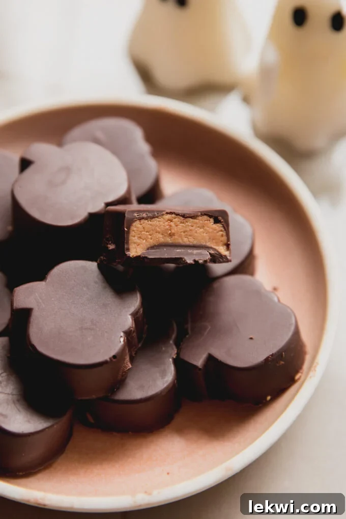Almond butter cups shaped like pumpkins on a pink plate, with a bite taken from one, showing the creamy filling.