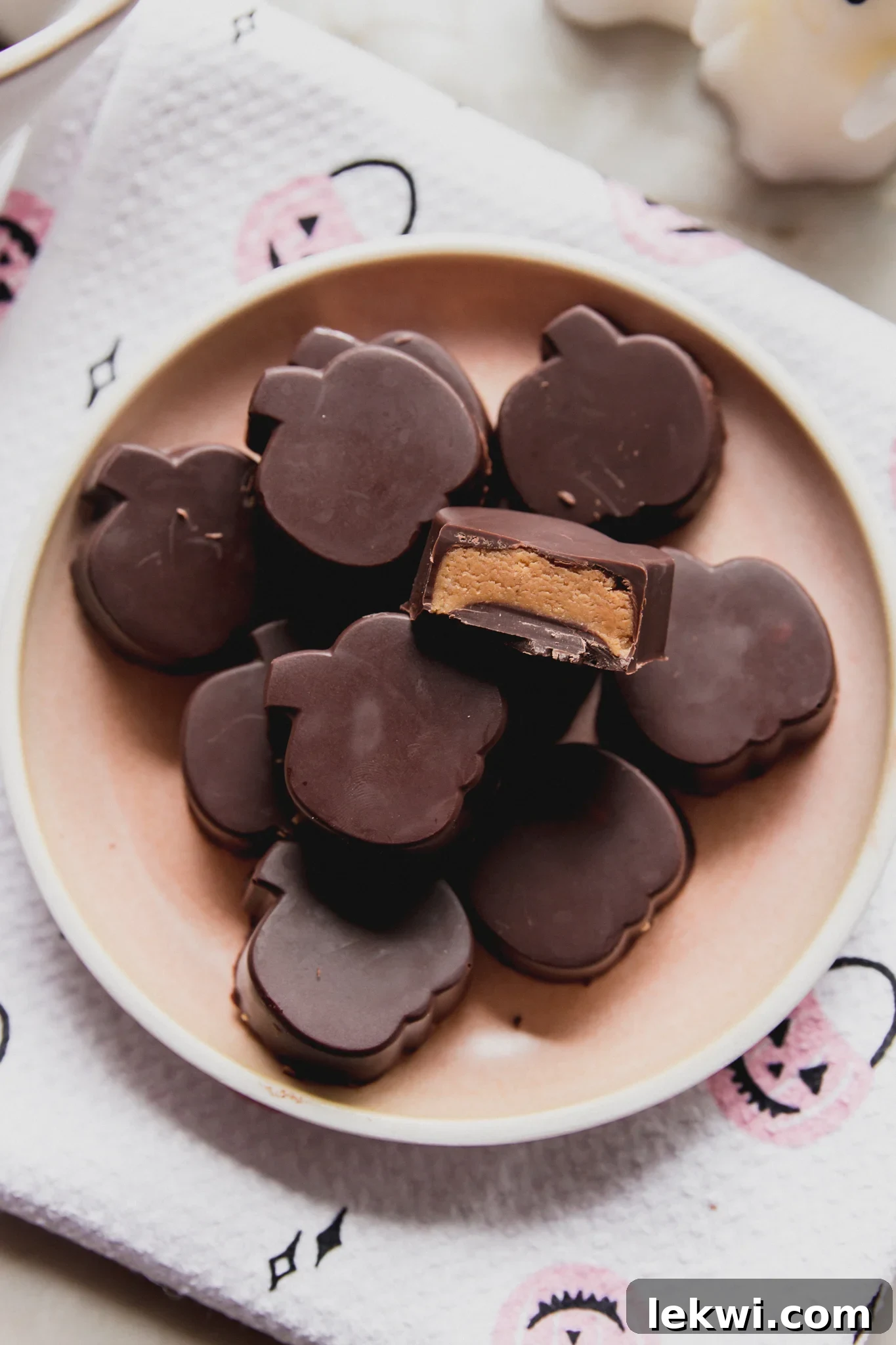 Almond butter cups shaped like pumpkins on a pink plate, with a bite taken from one.