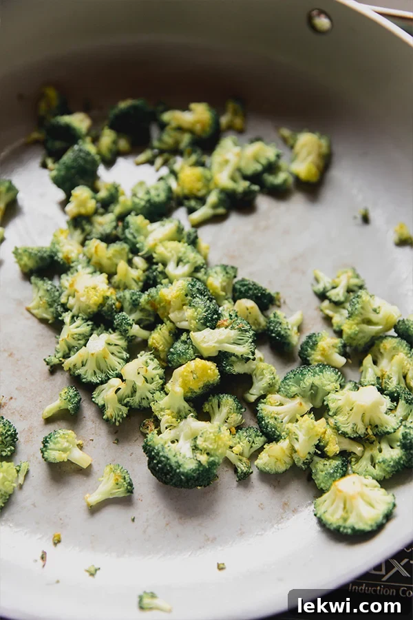 Fresh broccoli florets being expertly sauteed in a pan, vibrant green and lightly charred.