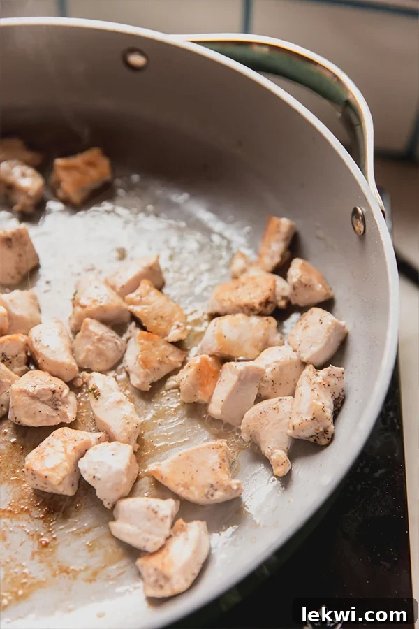 Perfectly diced and cooked chicken pieces, golden brown from sauteing, resting in a pan.