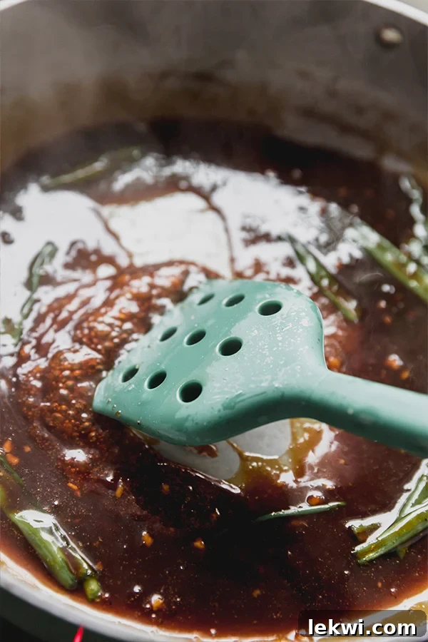Teriyaki sauce bubbling and simmering gently in a pan, being stirred with a green spatula.