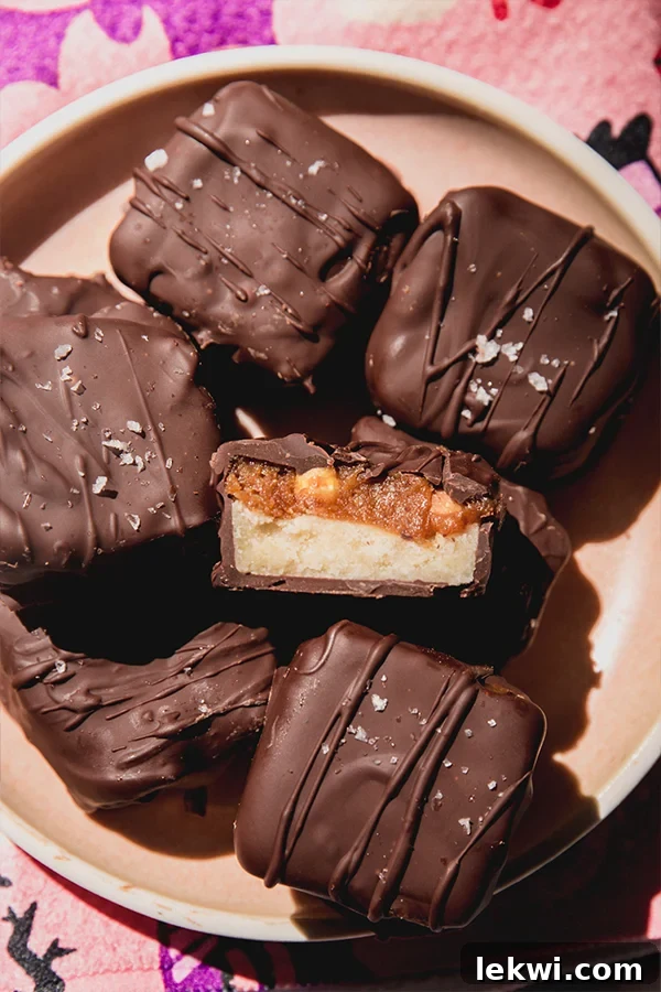 A plate of mini healthier Snickers bars, with one bar cut in half to reveal the distinct nougat, caramel, and peanut layers.
