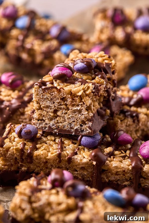 Delicious Kudos bars, featuring colorful candy toppings and delicate chocolate drizzles, neatly stacked with parchment paper in between, ready for storage.