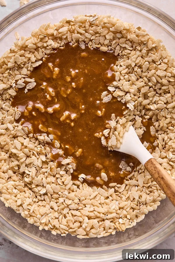 Rice cereal being gently mixed with the warm almond butter syrup mixture in a large bowl.