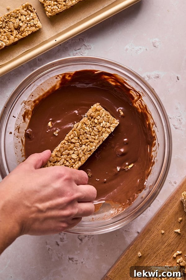 A Kudos bar base being carefully dipped into a bowl of smooth, melted chocolate.