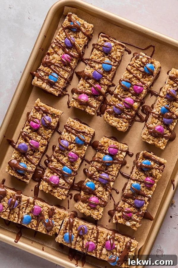 Freshly made Kudos bars, adorned with colorful candy and a generous chocolate drizzle, cooling on a baking sheet, awaiting their final set.