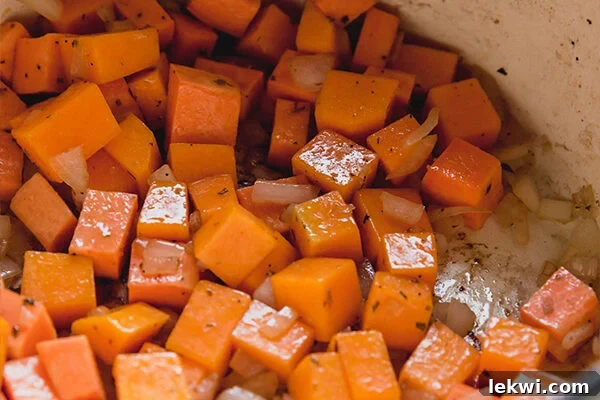 Diced sweet potato and onion gently cooking in a large, deep pot on the stovetop, releasing their aromatic flavors and beginning to soften, forming the flavorful base of the chili.
