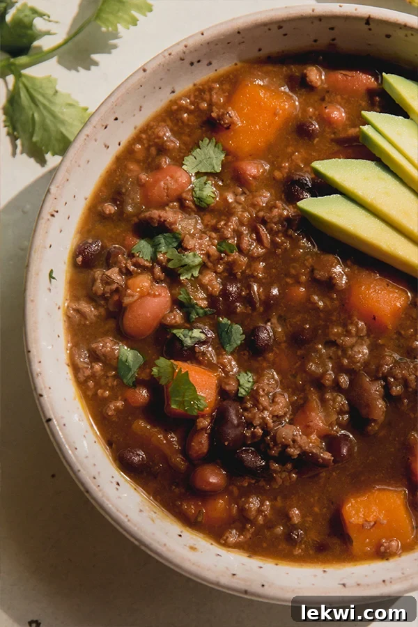 A close-up shot of a bowl of nightshade-free chili, beautifully garnished with fresh cilantro and vibrant avocado slices, emphasizing its inviting texture and delicious appeal, ready to be enjoyed.