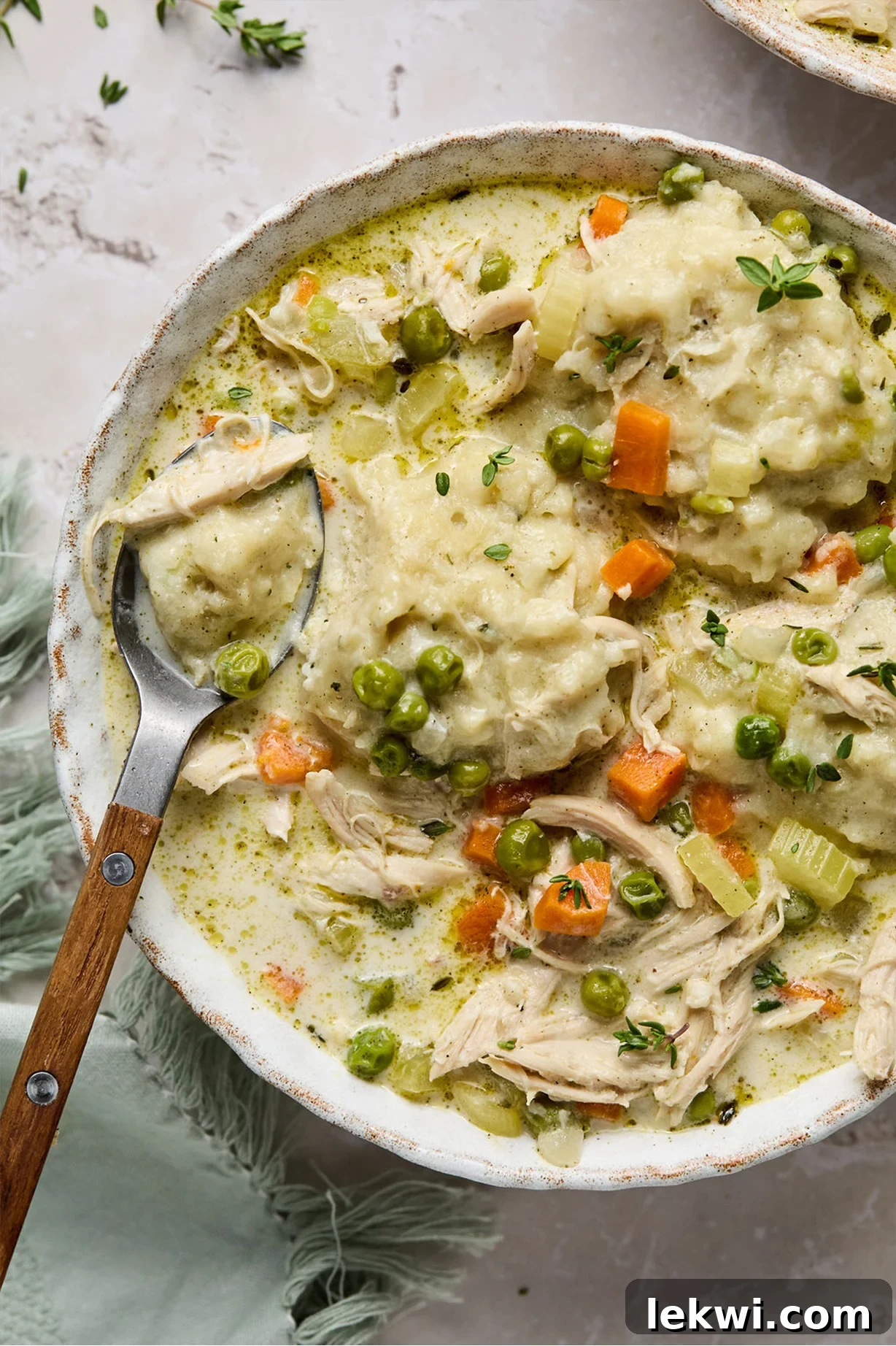 A bowl of creamy gluten-free chicken and dumplings, garnished with fresh herbs.