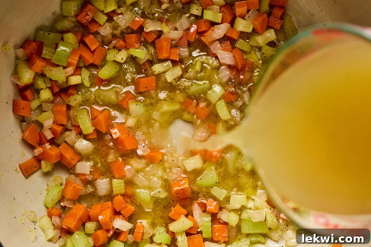 Celery, onion and carrot diced and ready in a bowl with broth pouring in.