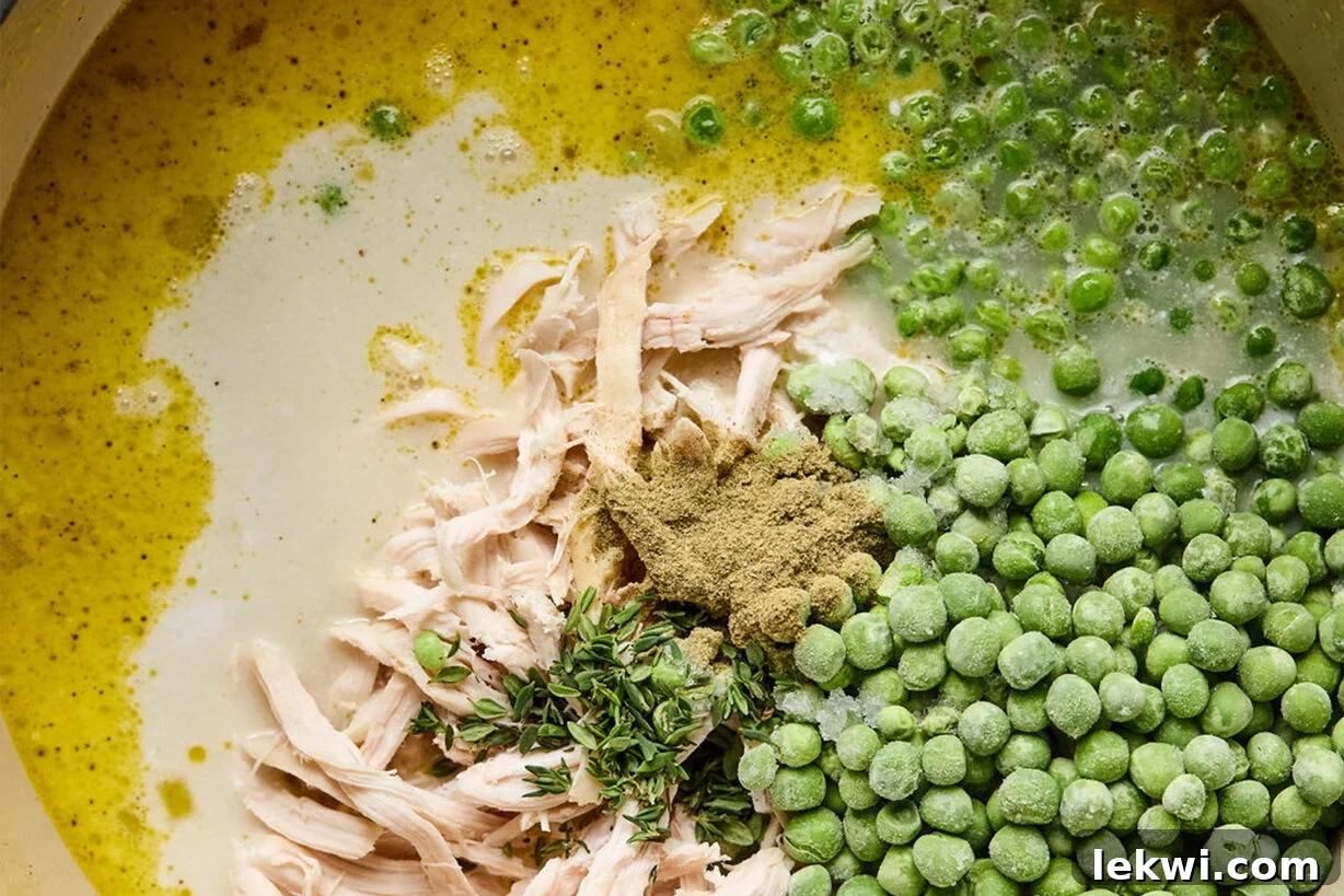 Shredded cooked chicken and frozen peas with herbs in a pot with broth.