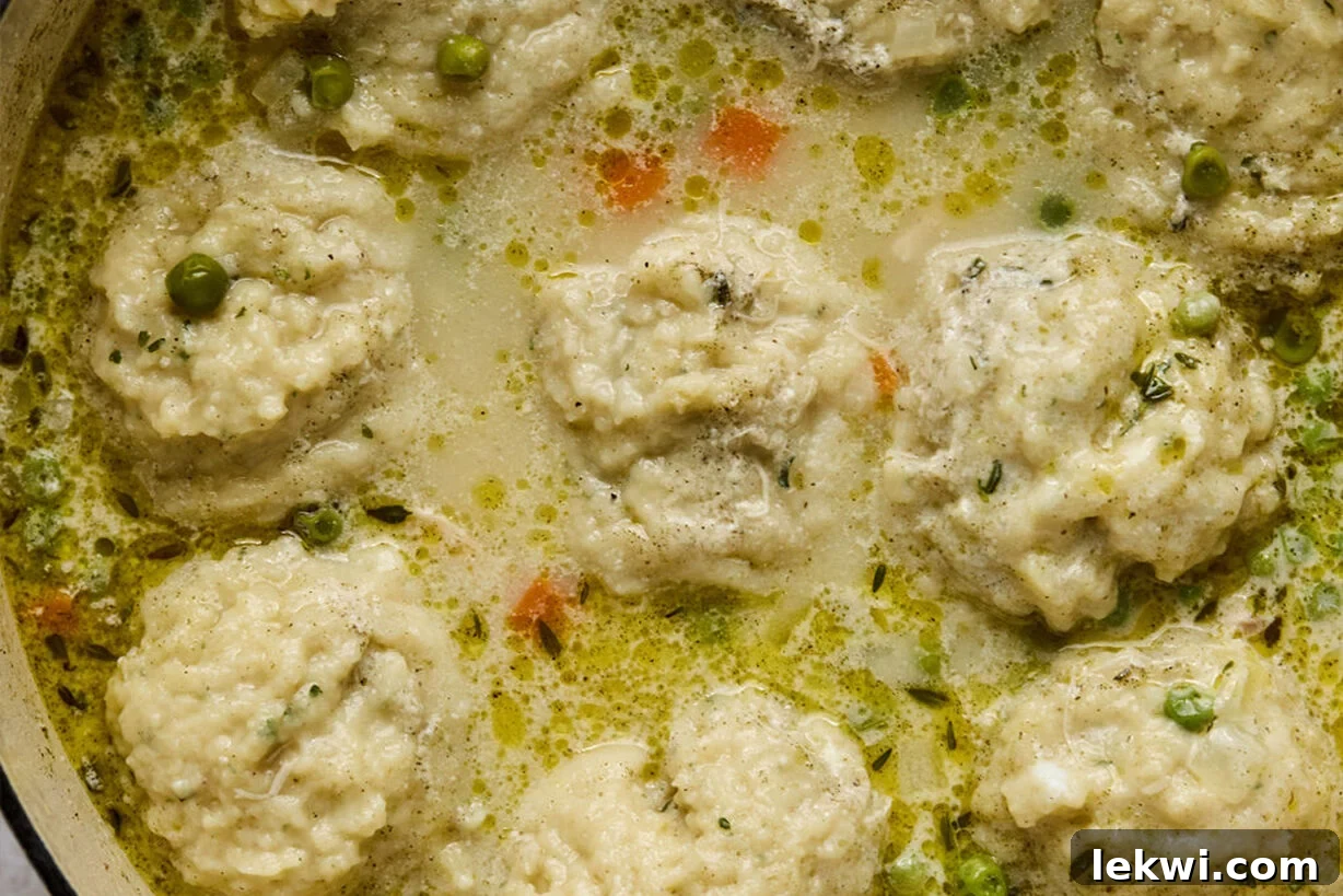 Cooked gluten-free dumplings floating in the creamy chicken soup, garnished with fresh herbs.