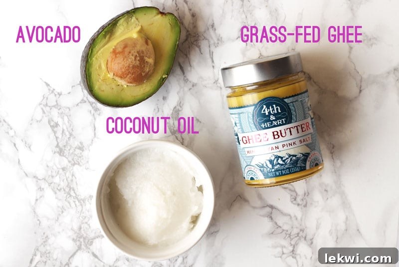 A selection of healthy fats including coconut oil, avocado, and ghee, presented on a marble background.