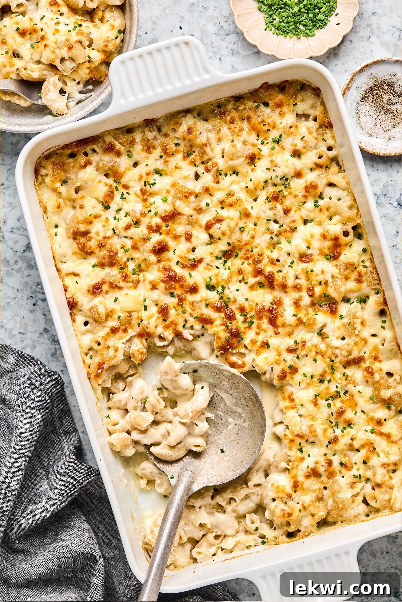 Goat cheese mac and cheese in a baking dish with a bowl of mac and cheese on the side.