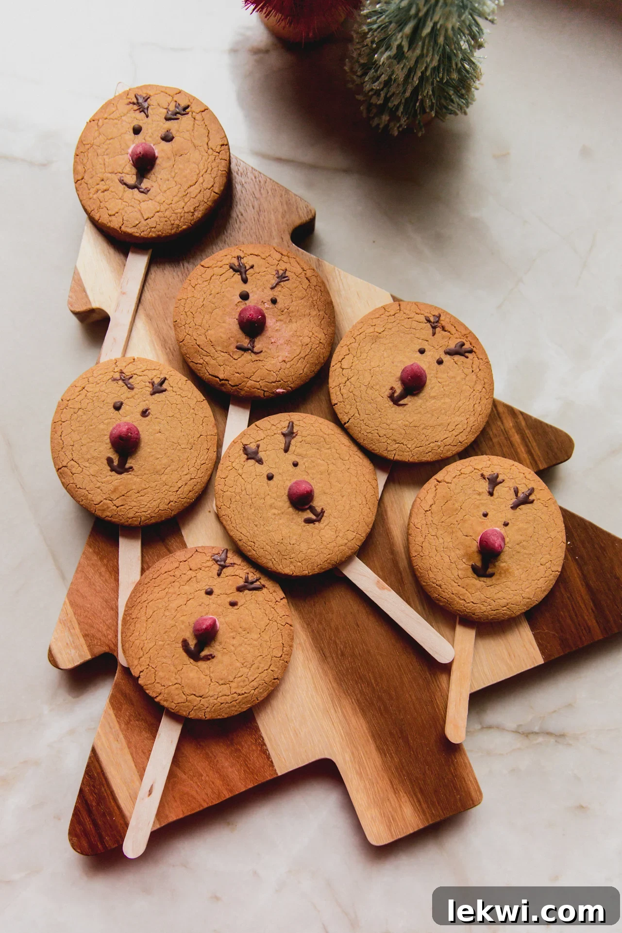Smiling gingerbread reindeer cookies with red noses and antlers, each featuring a popsicle stick.