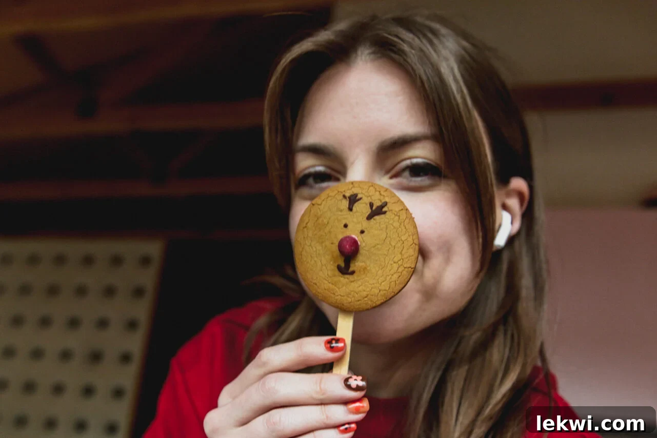 A person holding a gingerbread reindeer cookie up to their face, mimicking Rudolph.