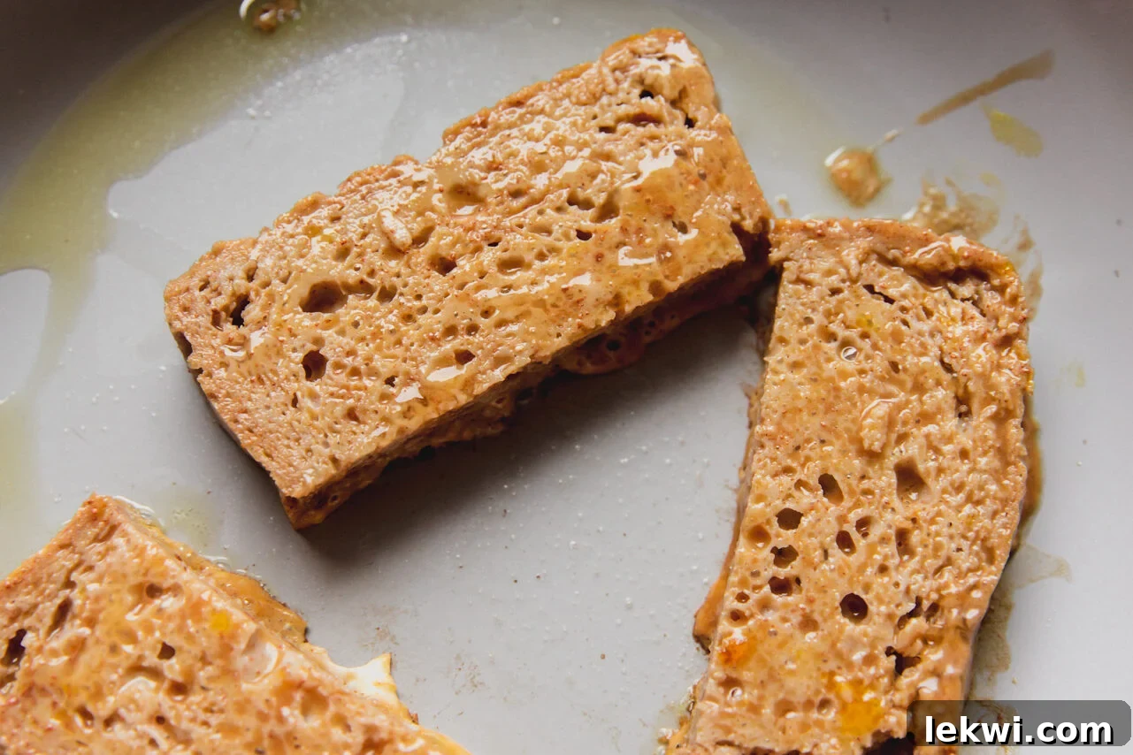 Several gluten-free French toast sticks sizzling in a hot pan, cooking to a perfect golden-brown crisp.