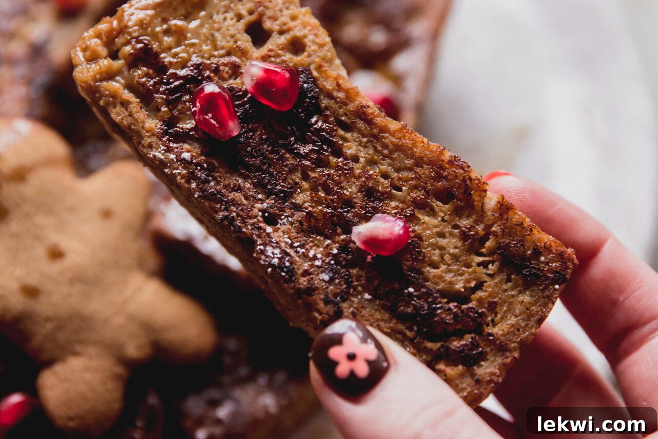 A plate of freshly cooked gluten-free French toast sticks, elegantly topped with glistening pomegranate seeds and a light dusting of powdered sugar.
