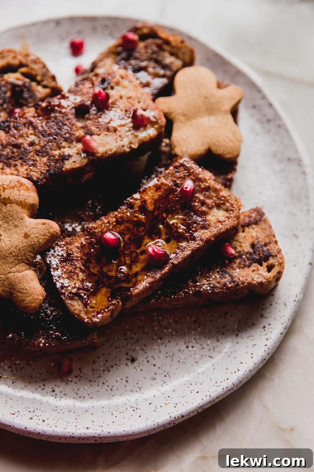Gluten-free gingerbread French toast on a plate topped with pomegranate seeds and maple syrup.