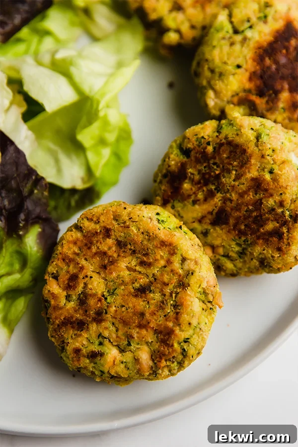 A white plate with a few golden-brown salmon cakes next to fresh lettuce, ready to be served.