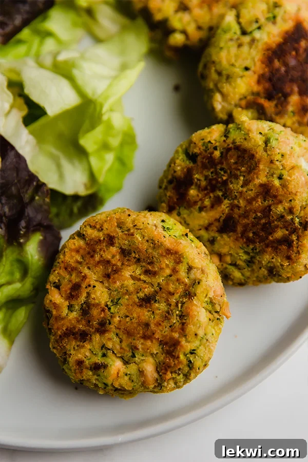 A white plate with a few salmon cakes next to lettuce.
