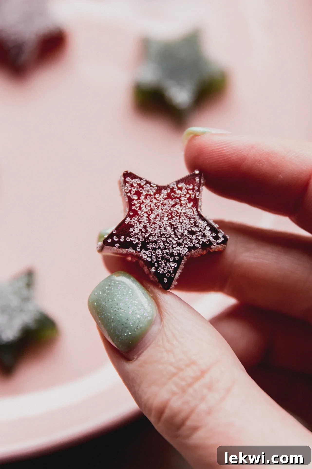 A single, perfectly formed star-shaped gumdrop, vibrant and sugar-coated, is being picked up against a festive background, showcasing its homemade charm and inviting texture.