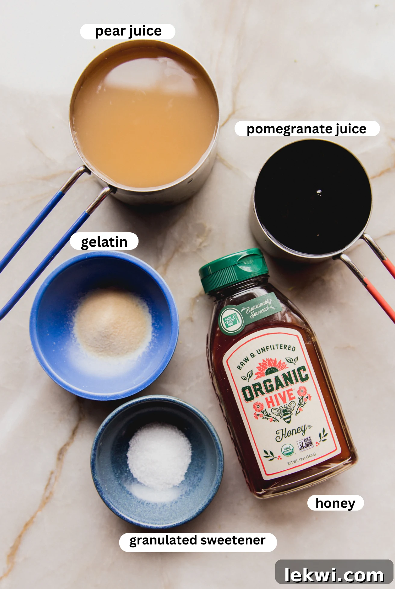 Various gumdrop ingredients, including bottles of pear and pomegranate juice, a jar of honey, and a bowl of gelatin powder, neatly arranged in separate bowls on a light surface.