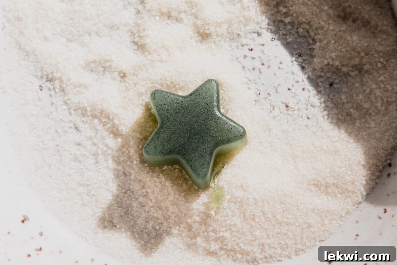 A freshly dried green star-shaped gumdrop is gently placed into a bowl filled with granulated sweetener, ready to be coated.